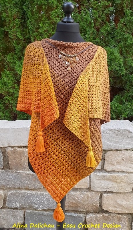 Gehäkeltes Dreieckstuch in Braun‑Orange‑Farbverlauf mit drei Quasten auf einer Schneiderpuppe vor einer Steinmauer