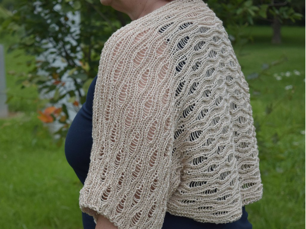 Seitliche Ansicht eines beigen, gestrickten Boleros mit Ajourmuster über dunklem Oberteil