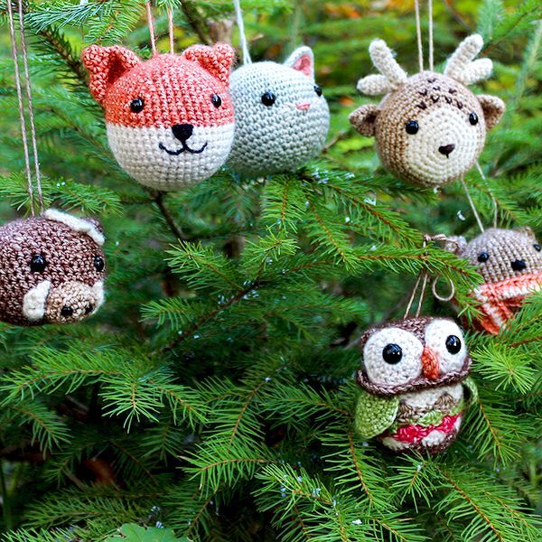 Mehrere gehäkelte Tiergesichter als Kugel-Anhänger in Tannenzweigen, darunter Fuchs, Katze, Rentier und Eule