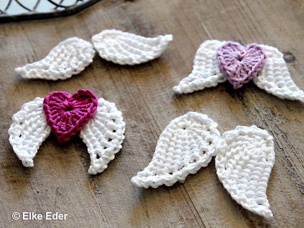 White crocheted angel wing appliques with small pink and purple hearts on a wooden table