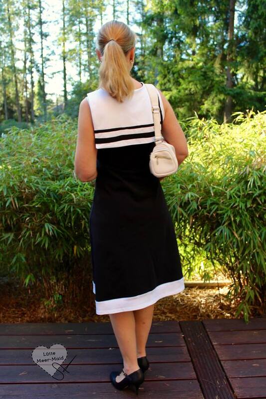 Frau von hinten in zweifarbigen, ärmellosen Kleid mit weißen und schwarzen Elementen vor natürlichem Hintergrund