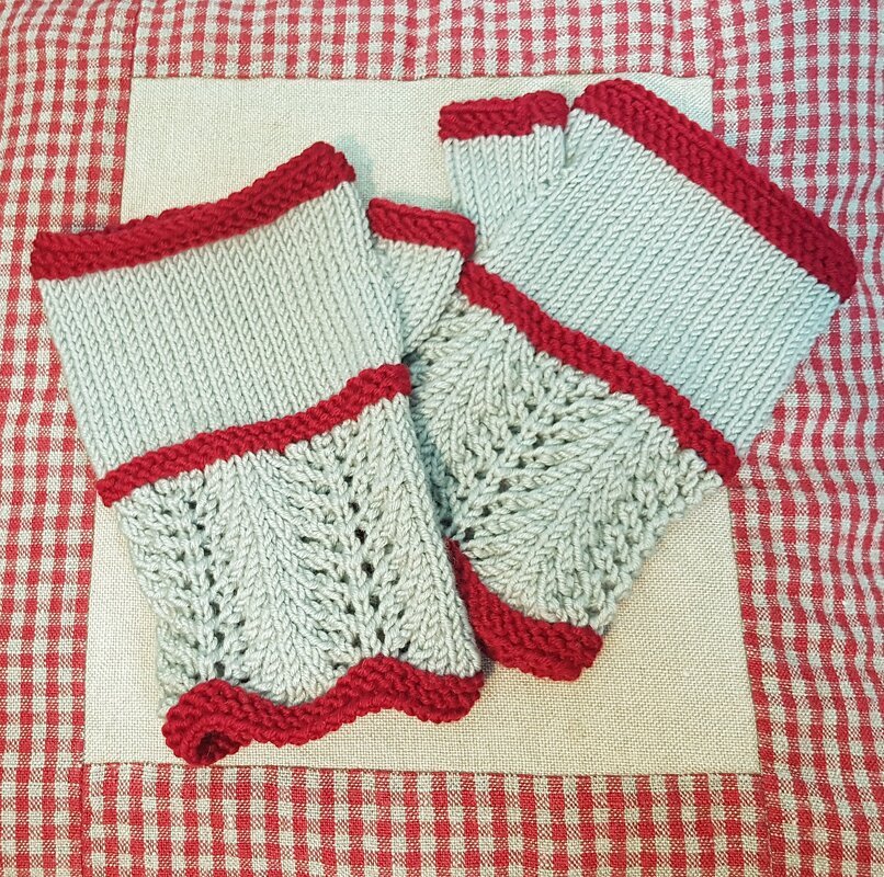 Zwei hellgraue gestrickte fingerlose Handschuhe mit rotem Rand und Lochmuster.