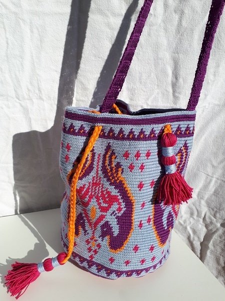 Gehäkelte Umhängetasche in Hellblau mit lila-pinken Ornamenten, orangefarbenem Tunnelzug und Quasten