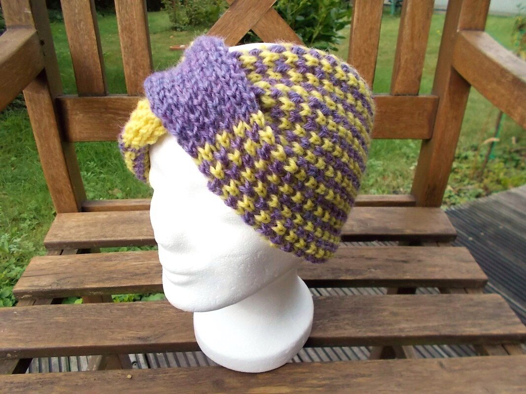 Schaufensterkopf mit gestricktem Stirnband in Lila und Gelb mit gedrehter Vorderseite auf Holzbänkchen