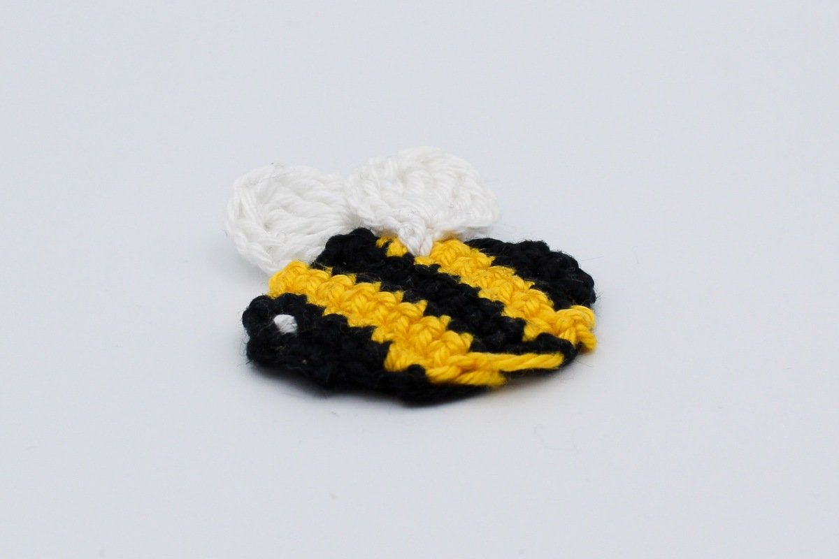 Von oben sichtbare gehäkelte Biene mit gelb-schwarzem Körper und zwei weißen Flügeln.