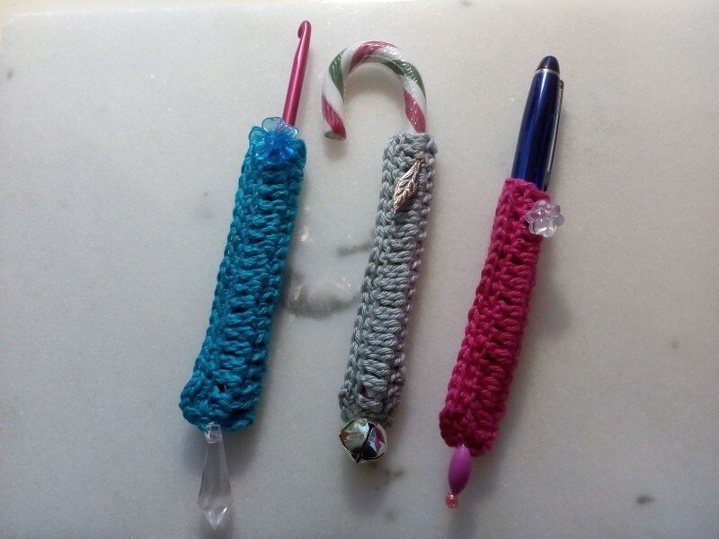 Drei schlanke gehäkelte Röhren als Hüllen für Stifte, Häkelnadel und Zuckerstange mit Perlen, Blatt und Kugel