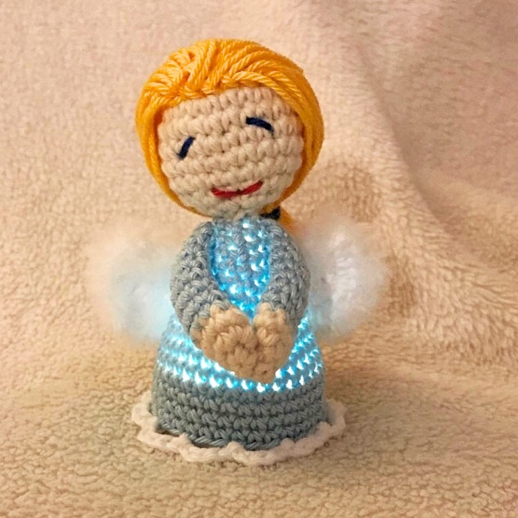 Gehäkeltes Amigurumi‑Engelchen mit leuchtendem blauem Kleid und weißen Flügeln