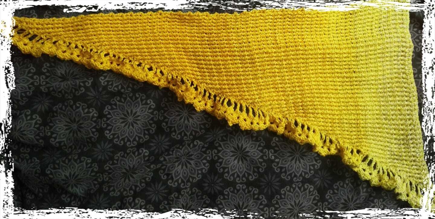 Gelbes, dreieckiges Häkeltuch mit durchbrochenem Zierrand auf dunklem, gemustertem Stoff