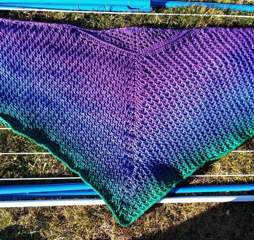 Gehäkeltes Dreieckstuch mit Farbverlauf Lila zu Türkisgrün auf Wäscheständer im Gras