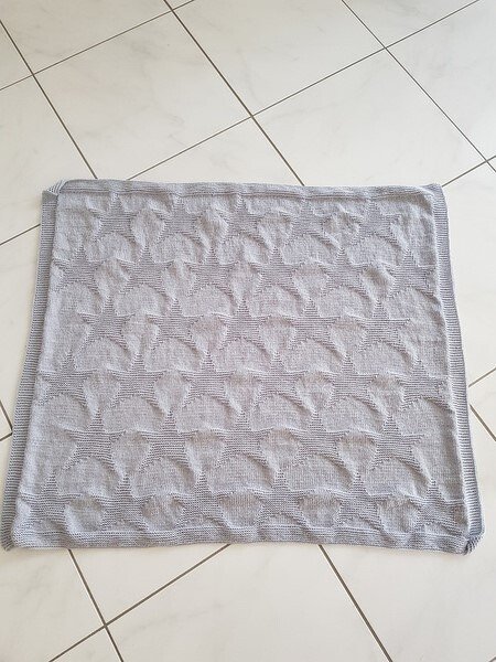 Hellgraue gestrickte Babydecke mit erhabenem Muschel- oder Fächermuster auf hellem Boden