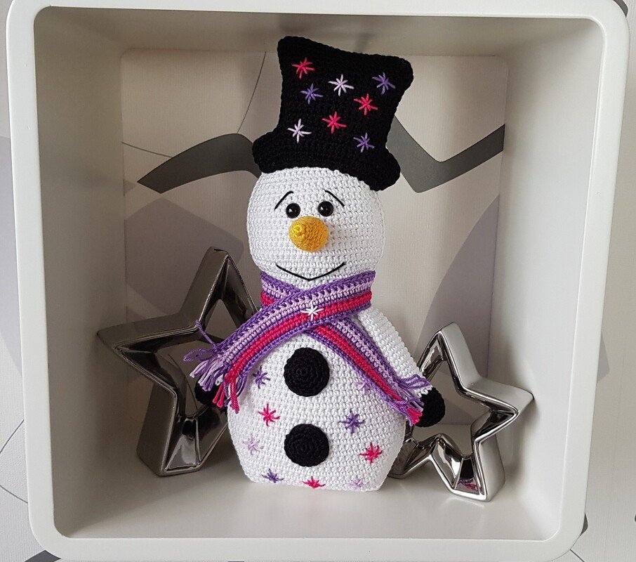 Gehäkelter Schneemann mit schwarzem Zylinder und lila-pinkem Schal in weißem Regalfach