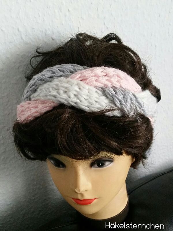 Gehäkeltes Stirnband mit Zopfmuster in Rosa, Weiß und Grau auf einer Schaufensterpuppe.