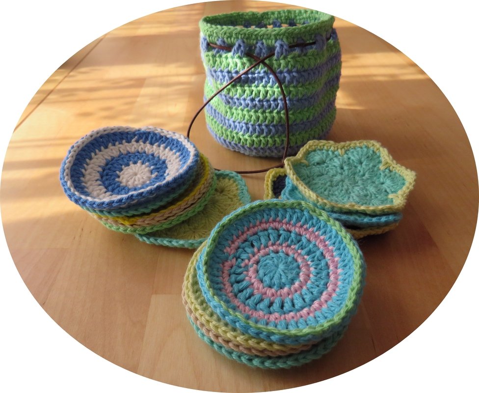 Gestapelte runde und blütenförmige gehäkelte Untersetzer neben einem gestreiften Aufbewahrungskorb mit Kordel auf Holztisch