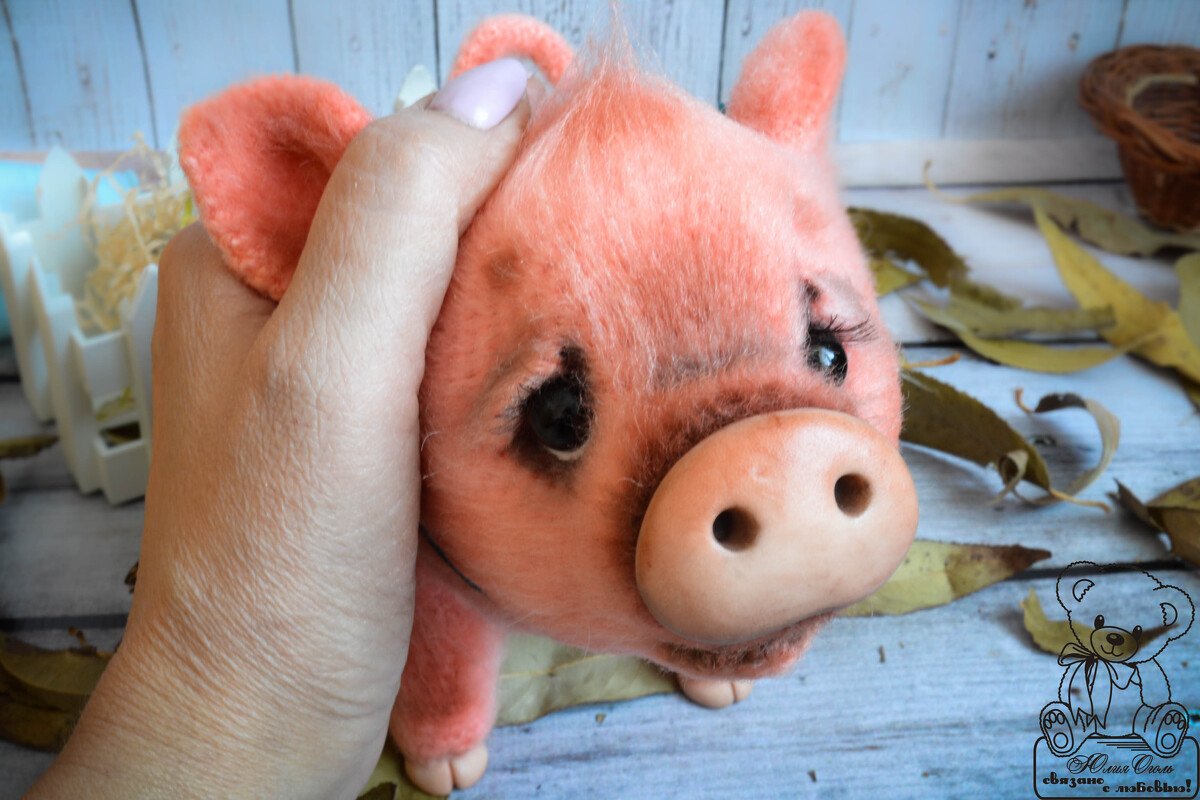 Hand holding a pink crochet amigurumi pig with a round snout and dark eyes