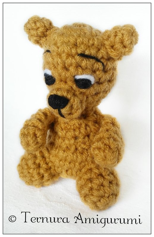 Detailaufnahme eines kleinen gehäkelten Amigurumi-Teddybären mit sichtbaren Maschen und gestickten Augen