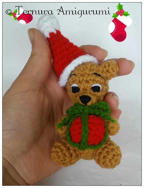 Mini amigurumi teddy bear in hand wearing a Santa hat and holding a tiny gift