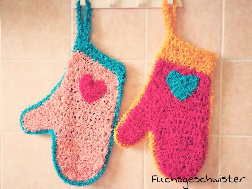 Zwei gehäkelte Topflappen in Fäustling‑Form mit Herz‑Applikationen an Haken
