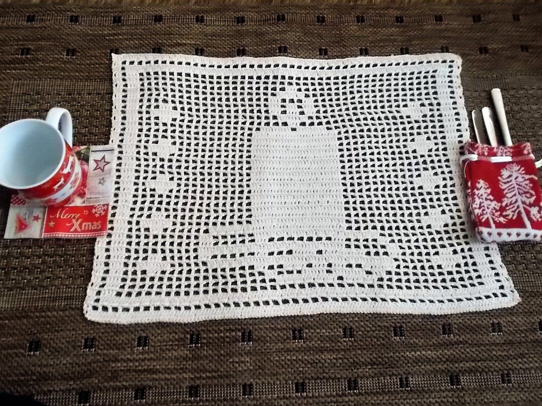 Weißes gehäkeltes Deckchen mit Kerzen- und Sternenmuster, links eine rote Tasse, rechts ein rotes Täschchen mit Besteck auf braunem Untergrund.
