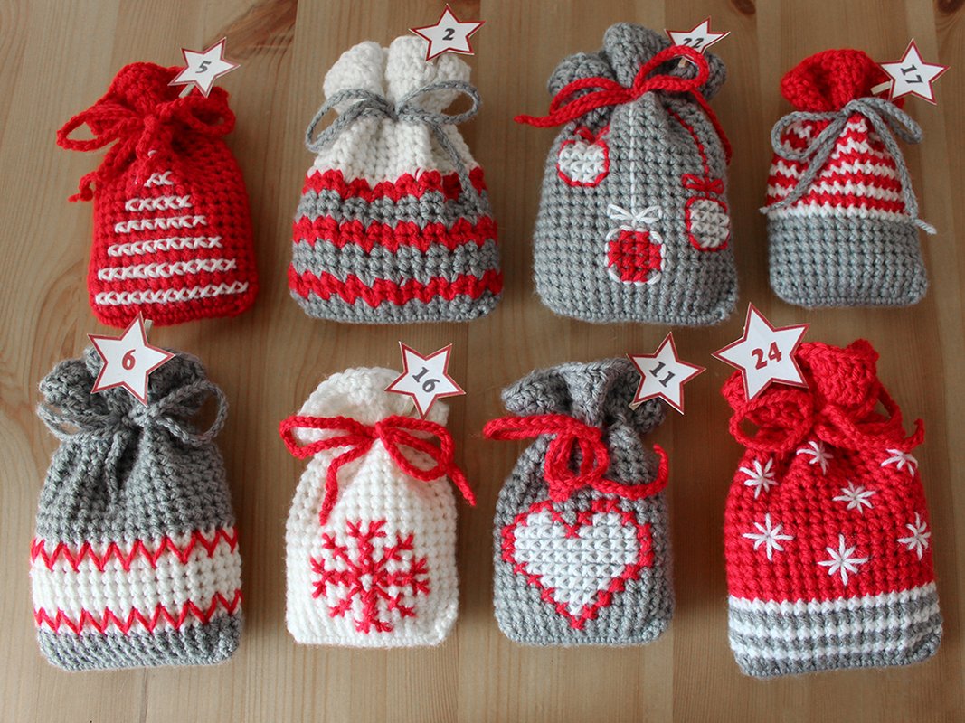 Eight crocheted Advent calendar bags in red, white, and grey with star-shaped number tags (visible numbers include 2, 5, 6, 11, 16, 17, 22, 24).