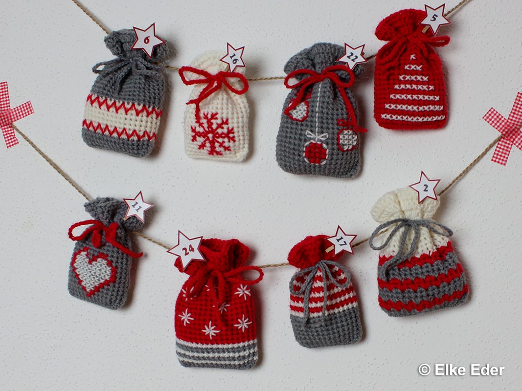 Acht gehäkelte Adventssäckchen in Rot, Grau und Creme mit Weihnachtsmotiven und nummerierten Sternchen an einer Schnur