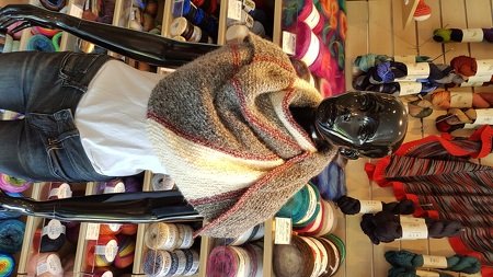 Schwarze Schaufensterpuppe trägt gestricktes halbrundes Tuch in Grau, Weiß und Braun mit roten Streifen