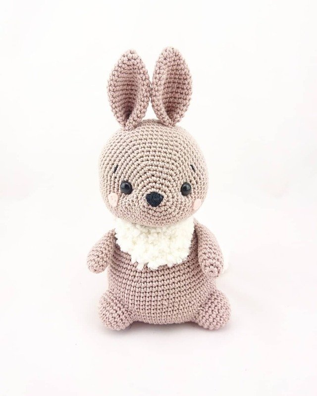 Gehäkelter rosa Hase mit weißem flauschigem Kragen vor hellem Hintergrund.