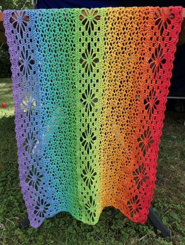 Rectangular ombre rainbow crocheted shawl with floral openwork patterns.