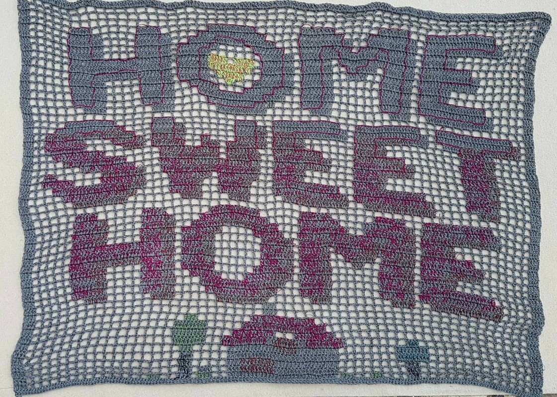Gehäkeltes Filetbild mit Schrift 'HOME SWEET HOME', graues Netz, pink-violette Buchstaben, gelbes Herz und kleines Häuschen