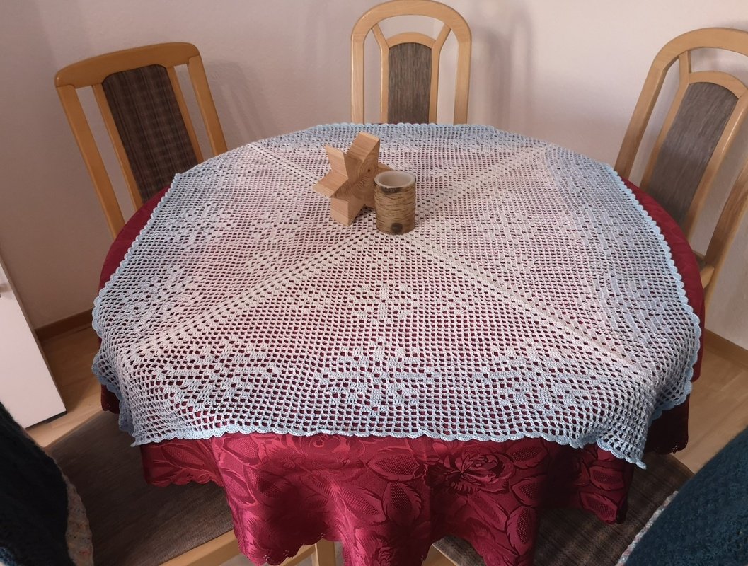 Rundes hellblaues gehäkeltes Deckchen mit Blumenmuster auf rotem Tisch