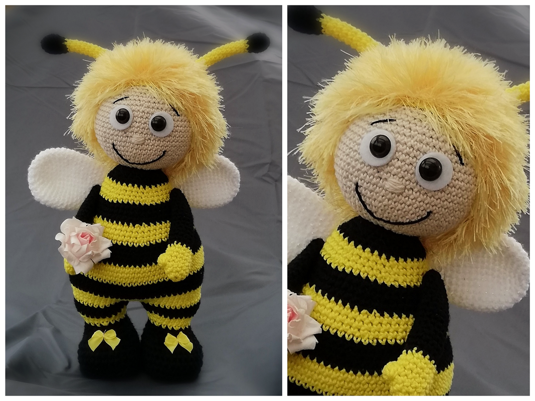 Gehäkelte gelb‑schwarze Bienen‑Amigurumi‑Puppe mit flauschigem Haar, weißen Flügeln und Rose