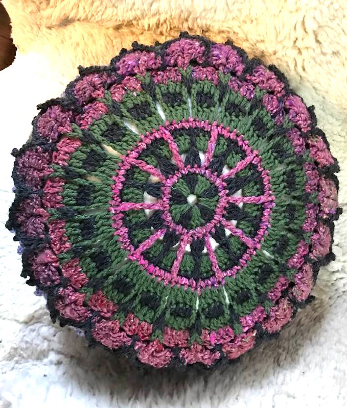 Rundes gehäkeltes Kissen mit detailreichem Mandala‑Muster in Grün und Pink mit dunkler Umrandung