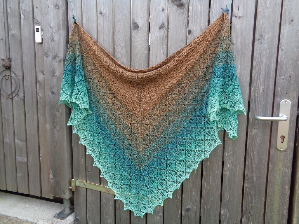 Gestricktes Dreieckstuch mit Farbverlauf von Braun zu Türkis, Ajourmuster und gezacktem Rand, an Holztür hängend
