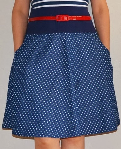 Dunkelblauer A-Linien-Rock mit weißen Punkten, rotem Gürtel und Händen in den Taschen
