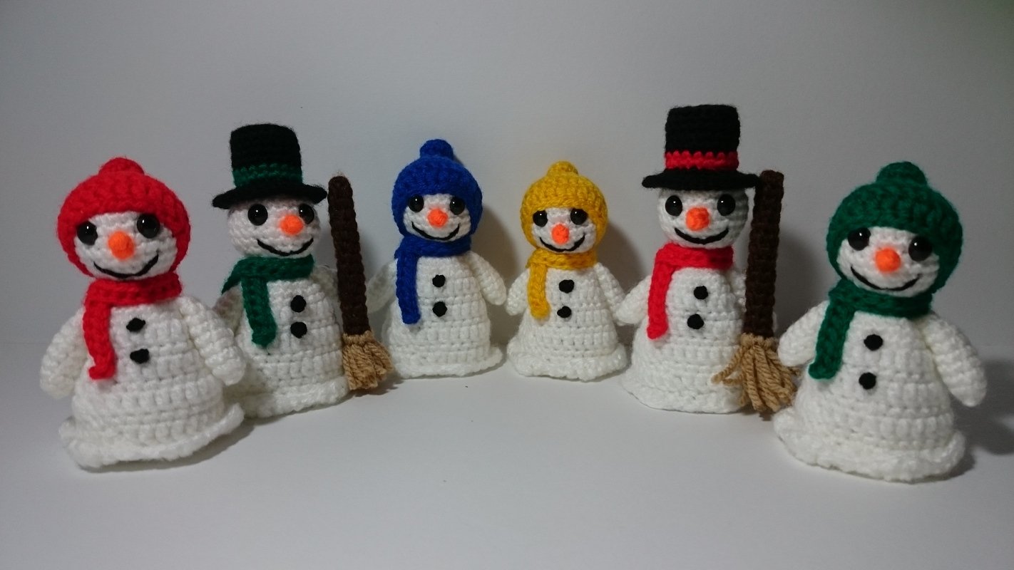 Sechs gehäkelte Schneemänner mit bunten Mützen und Schals, zwei mit Besen, vor hellem Hintergrund.