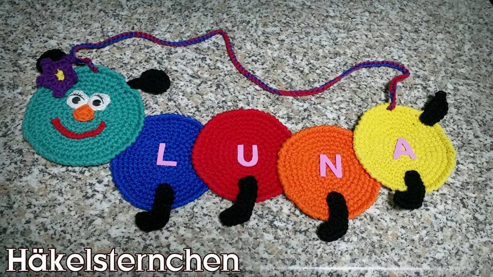 Gehäkelte Raupen-Namenskette LUNA mit fünf bunten Scheiben (türkis, blau, rot, orange, gelb) auf grauem Untergrund