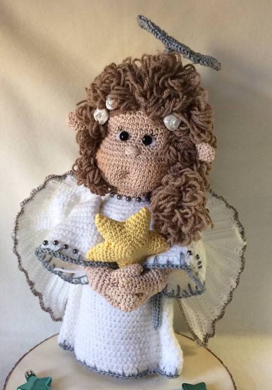 Nahaufnahme eines gehäkelten Amigurumi-Engels mit braunen Locken, weißem Kleid, Flügeln, Heiligenschein und gelbem Stern