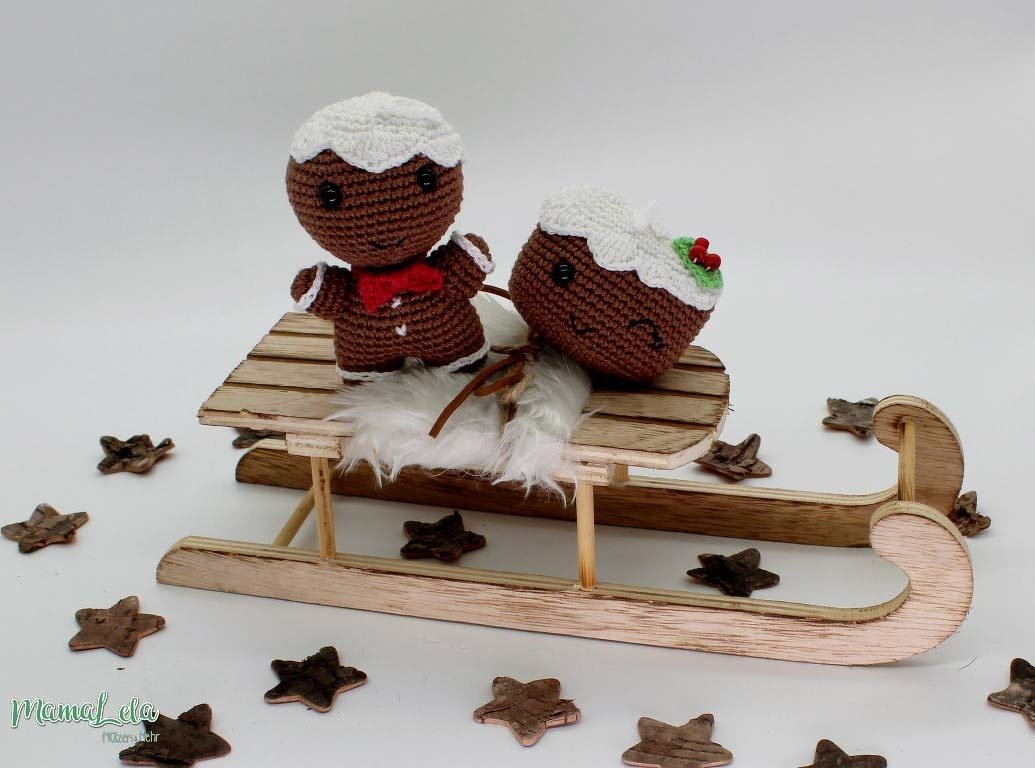Gehäkelter Lebkuchenmann und Weihnachtspudding auf einem Holzschlitten mit Sternen