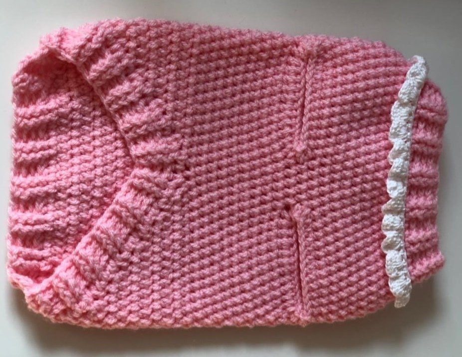 Rosa gehäkelter Hundepullover mit Rippenkragen und weißer Rüsche, flach liegend
