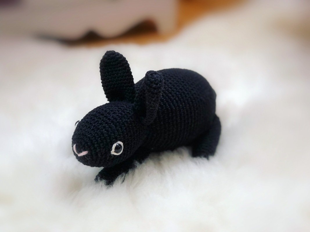 Schwarzer, gehäkelter Amigurumi-Hase auf weißem Fell