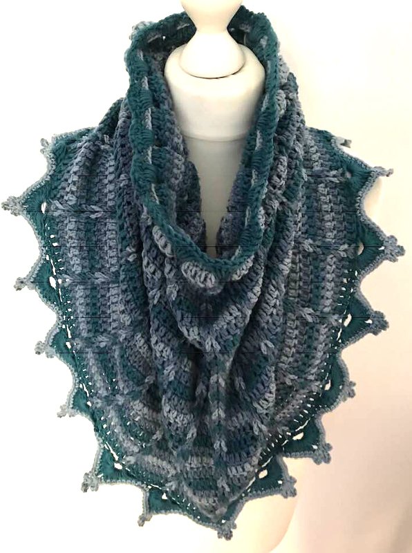 Gehäkelter Kragenschal in Blau, Türkis und Grau mit Zackenmuster am Saum, drapiert an einer Schaufensterpuppe.