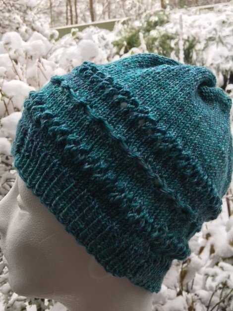 Türkisfarbene gestrickte Kinder-Beanie auf Schaufensterkopf vor verschneiter Kulisse