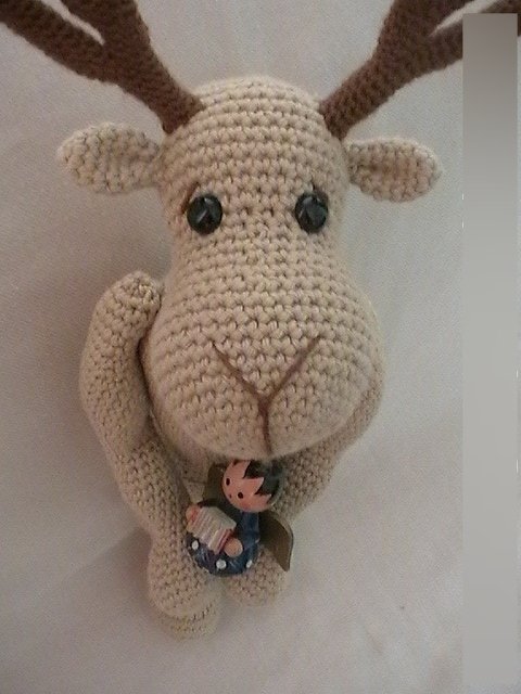 Gehäkeltes beiges Rentier-Amigurumi mit braunen Geweihen und kleiner Deko-Figur an der Vorderseite
