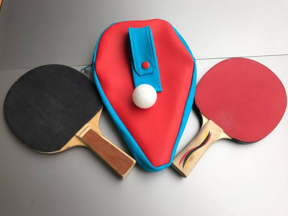 Rote und hellblaue genähte Schlägerhülle mit zwei Tischtennisschlägern und weißem Ball auf grauem Untergrund
