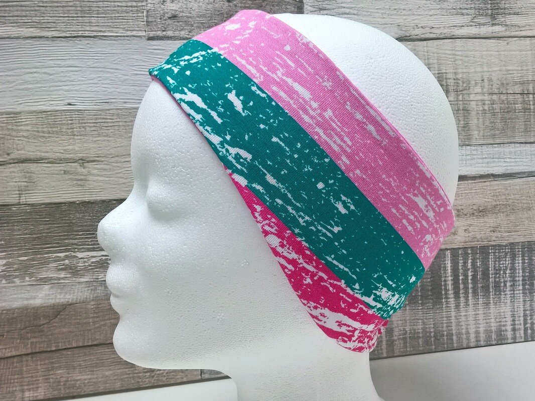 Gestreiftes Stirnband in Pink, Türkis und Magenta mit weißem Grunge-Muster auf weißem Mannequinkopf, Seitenansicht.