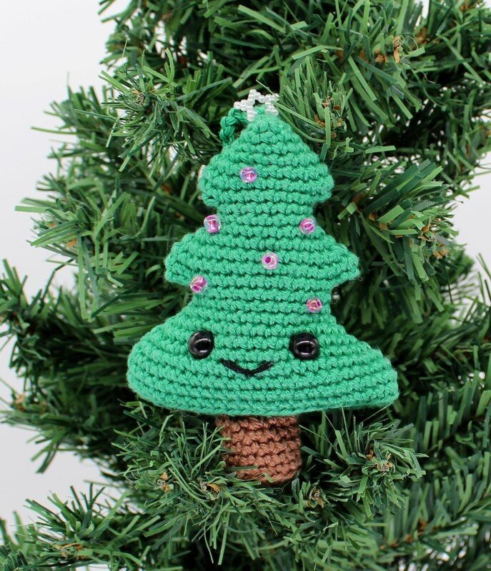Gehäkelter grüner Weihnachtsbaum-Anhänger mit lächelndem Gesicht, rosa Perlen und kleinem Stern, an einem Tannenzweig aufgehängt