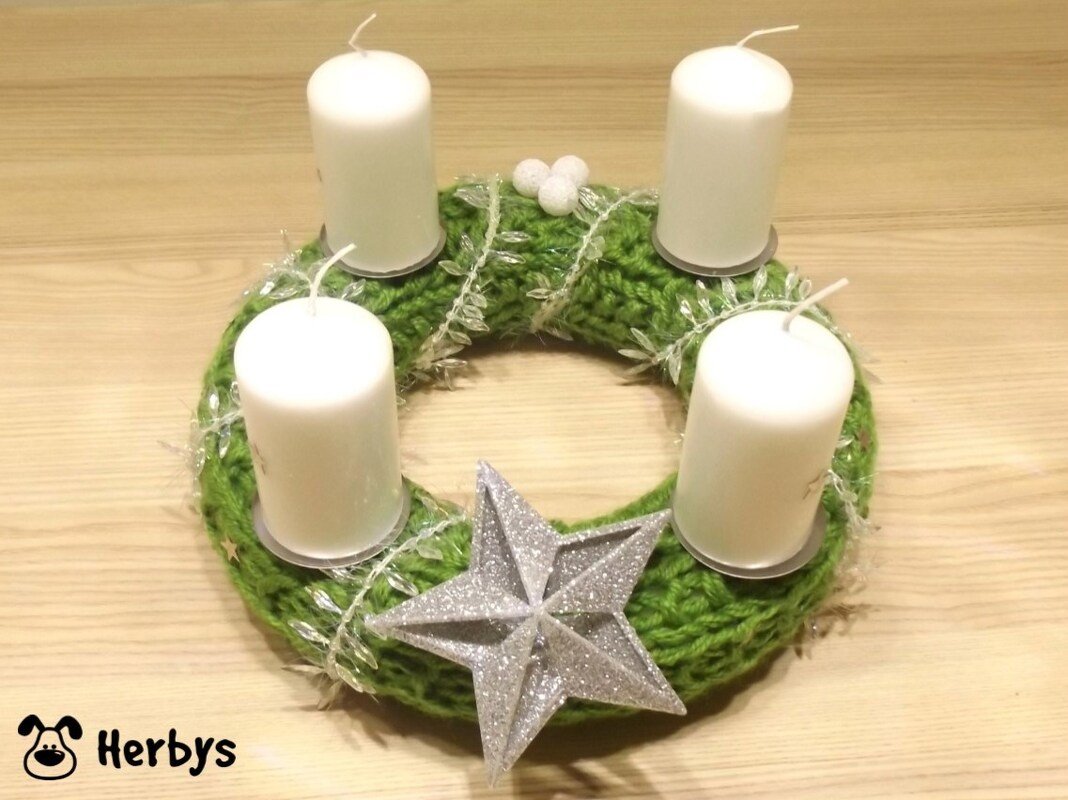 Gestrickter grüner Adventskranz mit vier weißen Kerzen und silbernem Stern auf hellem Holztisch