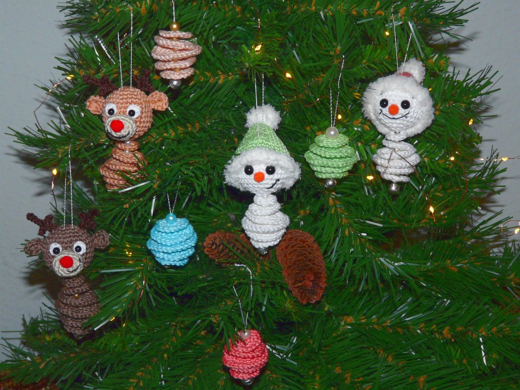 Nahaufnahme eines Weihnachtsbaums mit gehäkelten Rentier- und Schneemann-Anhängern sowie bunten spiralförmigen Kugeln.
