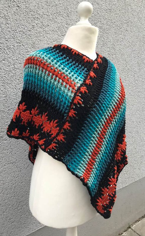 Häkelponcho mit luftigem Gittermuster, diagonalen Farbblöcken in Türkis/Blau, schwarzen Streifen und sternförmigen Reliefstichen am Rand.