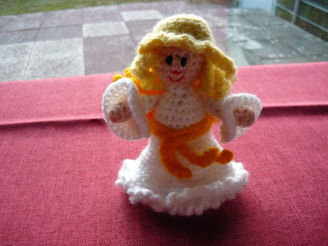 Gehäkelter Amigurumi-Engel mit weißem Kleid und gelbem Gürtel auf rotem Stoff