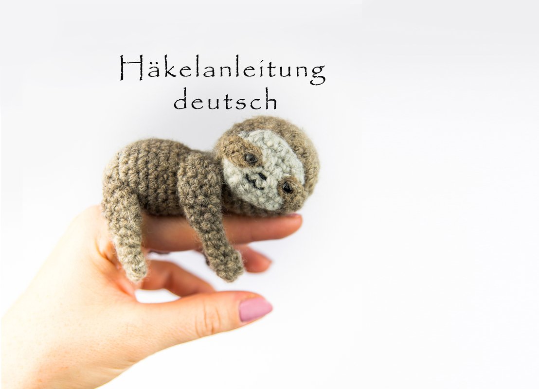 Gehäkeltes Faultier-Amigurumi auf einer Hand vor weißem Hintergrund